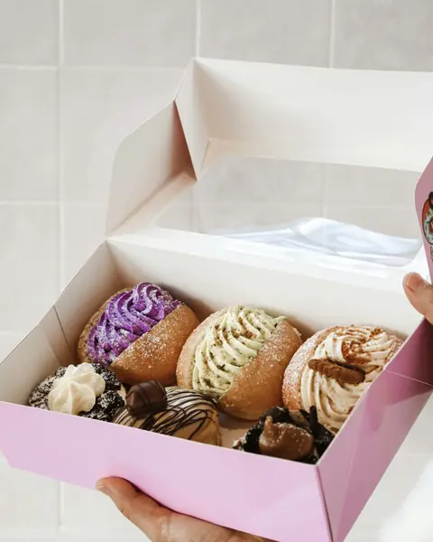 A person holding out an open bakery box of filled doughnuts